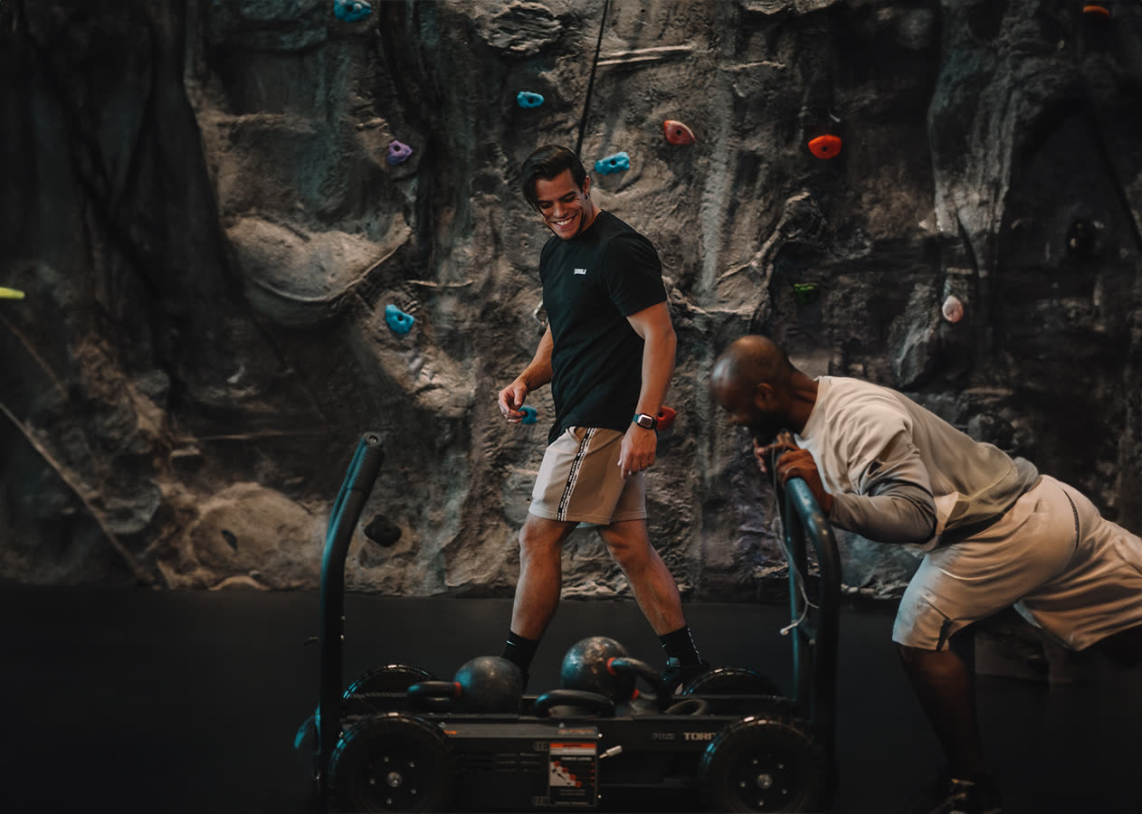 Coaching on the circuit floor — sled work with a trainer alongside