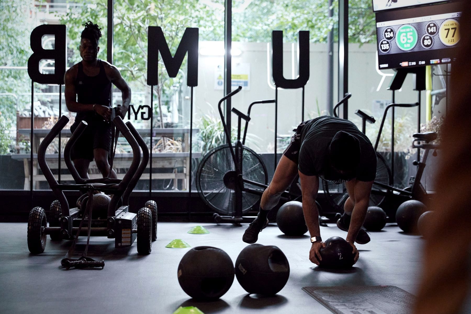 One member stands at the sled while another picks up a slam ball during a circuit class