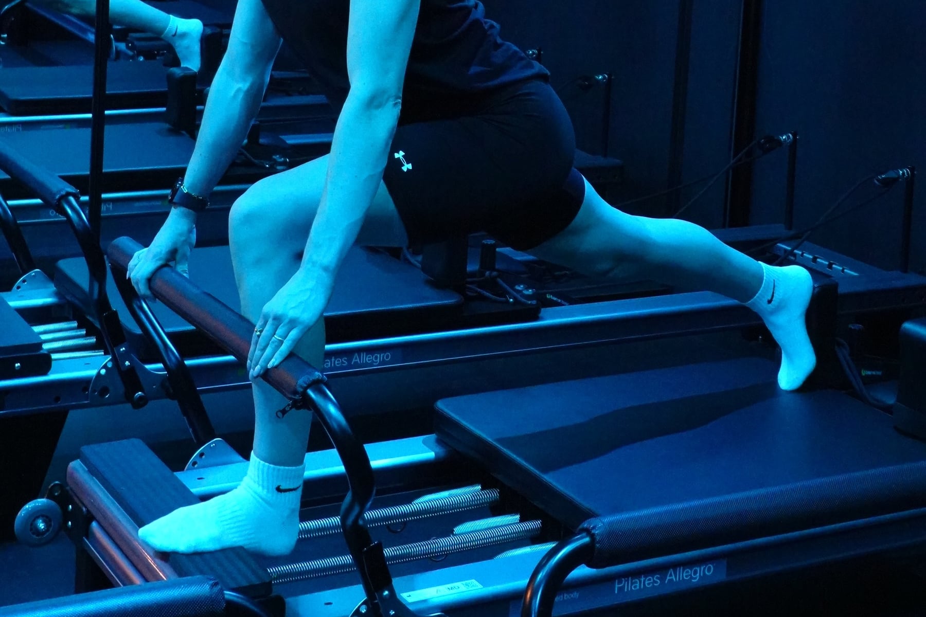 A member holds a standing lunge on the Reformer, hands resting on the frame