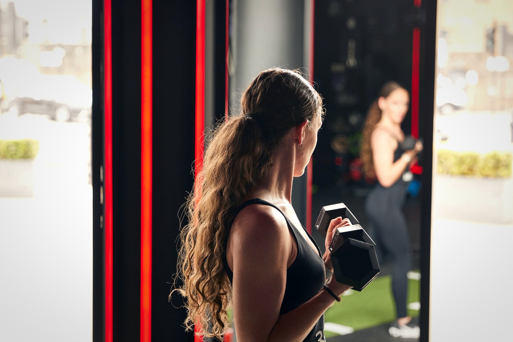 A woman checks her form in the mirror as she holds a dumbbell during a strength session at Rumble