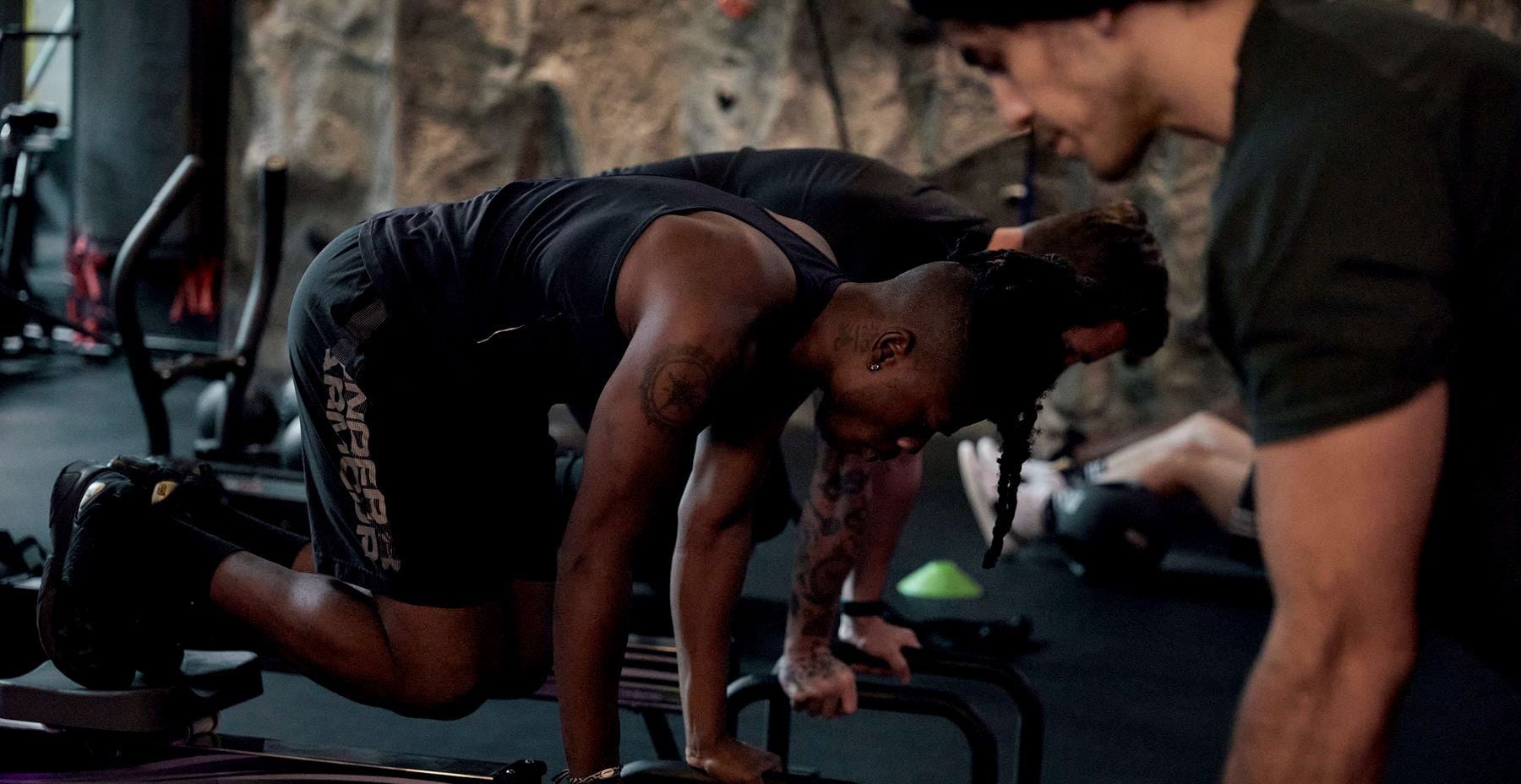 A coach leans in to cue a member’s push-ups on parallettes during the Re.HIIT circuit